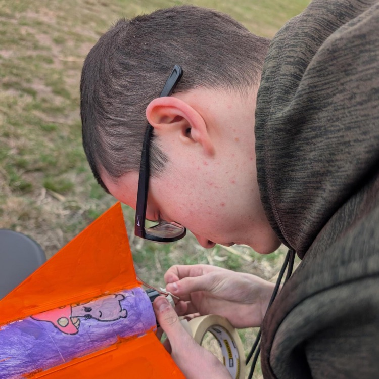 A male student looks closely as he tapes a section of the rocket together. 