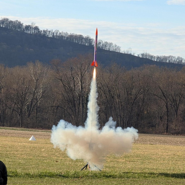 An orange and green rocket blasts off the platform into the air.