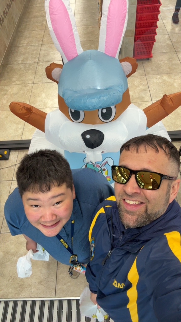 Coach Smith and a male student look up at the camera as they pose with a rabbit decoration.