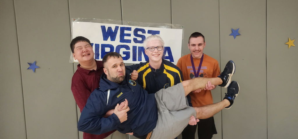 Male goalball players stand side-by-side as they hold up Coach Smith.
