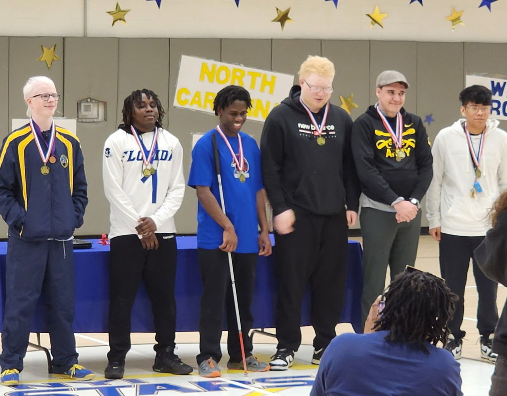 A group of male Goalball players stand in a line to receive their awards.