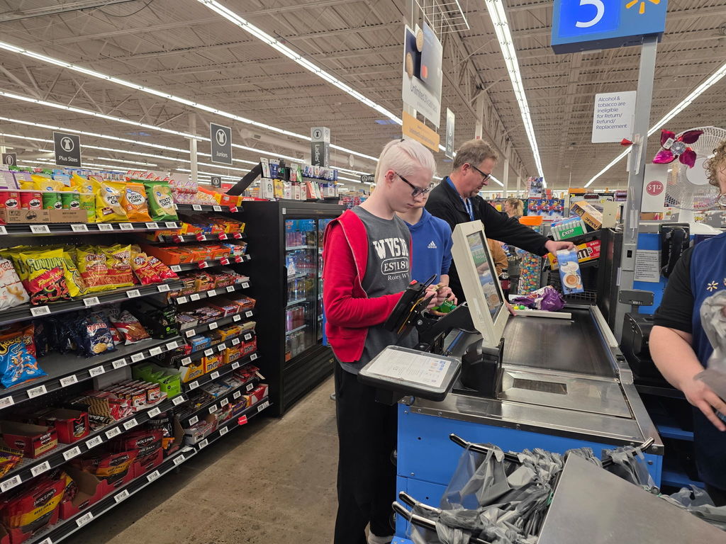 A male student is standing at the checkout. He has his wallet open to pay the cashier. 