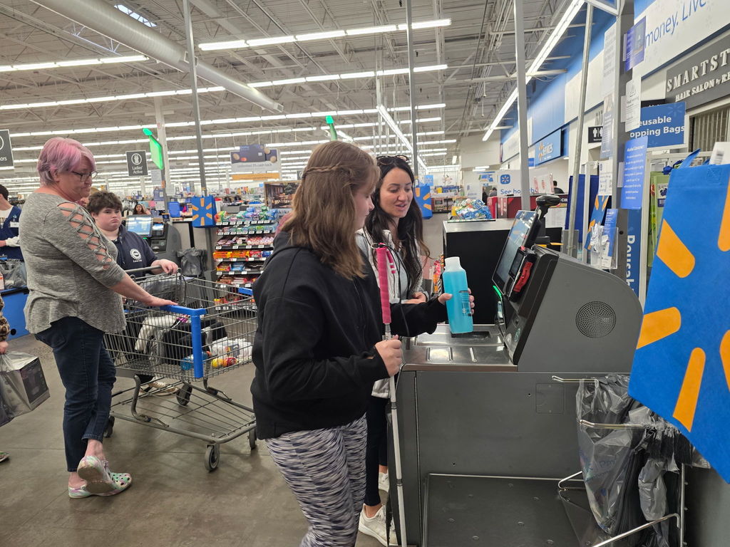 A female WVSDB representative assists a female student use the self-checkout.