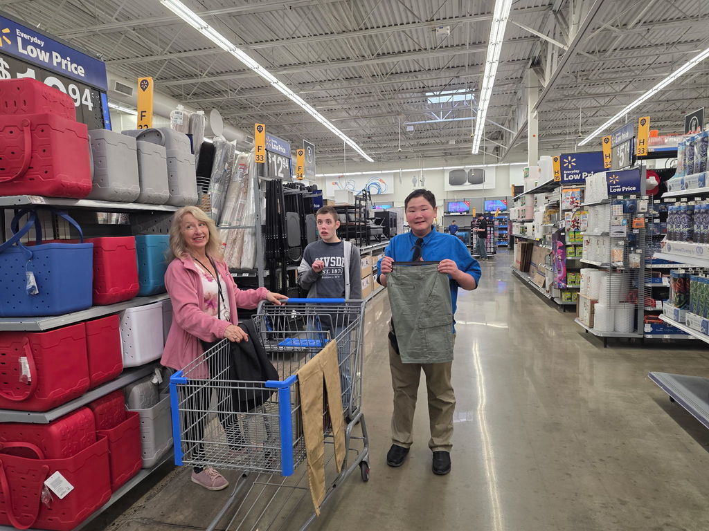 A female WVSDB representative smiles and holds onto a shopping cart while male students hold products they plan to purchase.