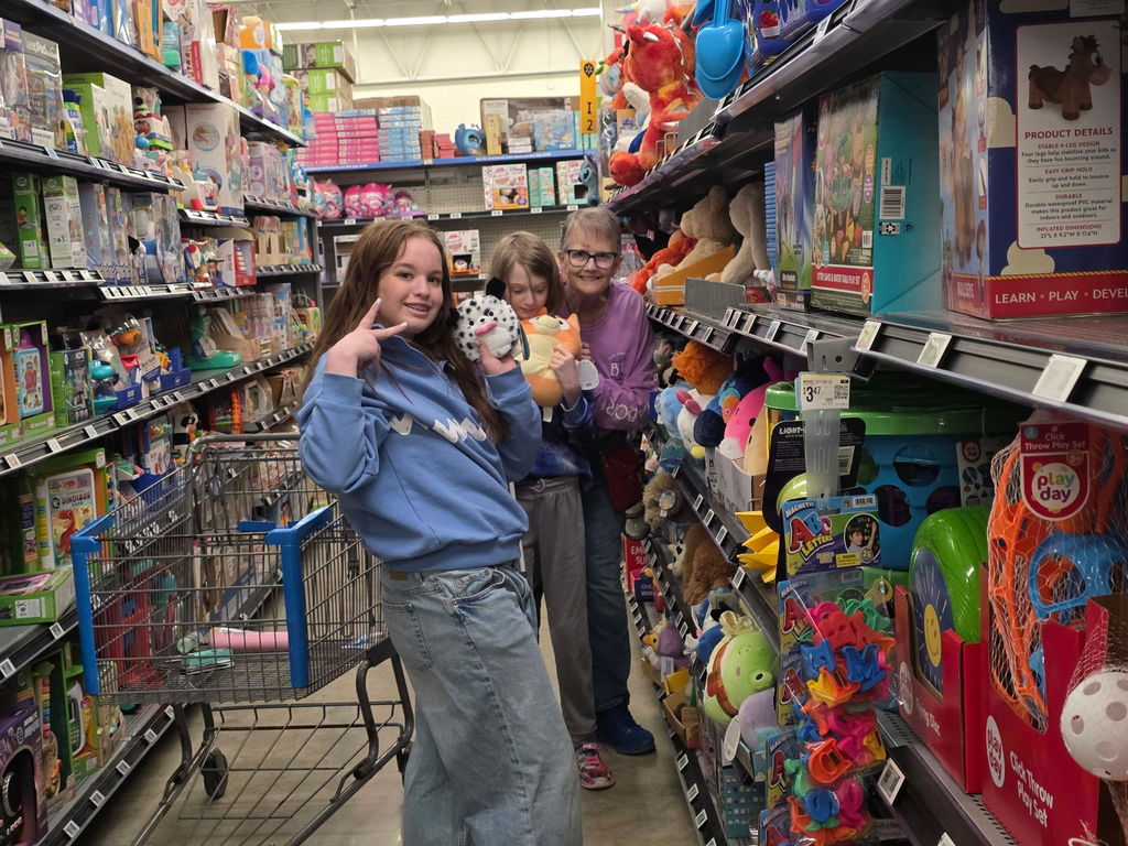 A female student smiles and holds up the "peace" sign with her hand. There are two females behind her smiling for the camera.