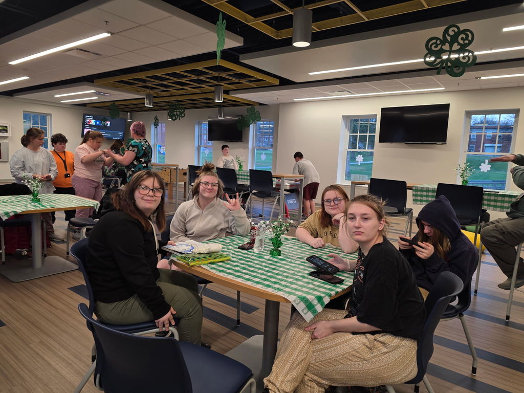 A group of female students are seated at a table with a green and white patterned tablecloth.