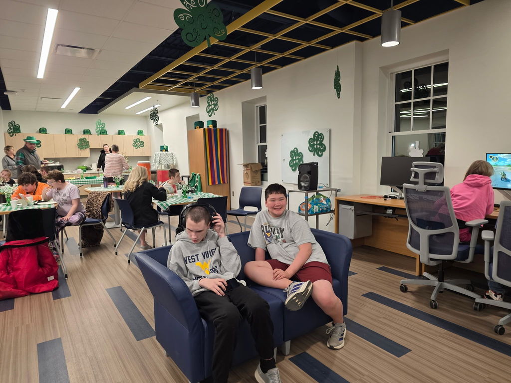 Two male students are seated on a blue-colored couch facing and smiling at the camera.