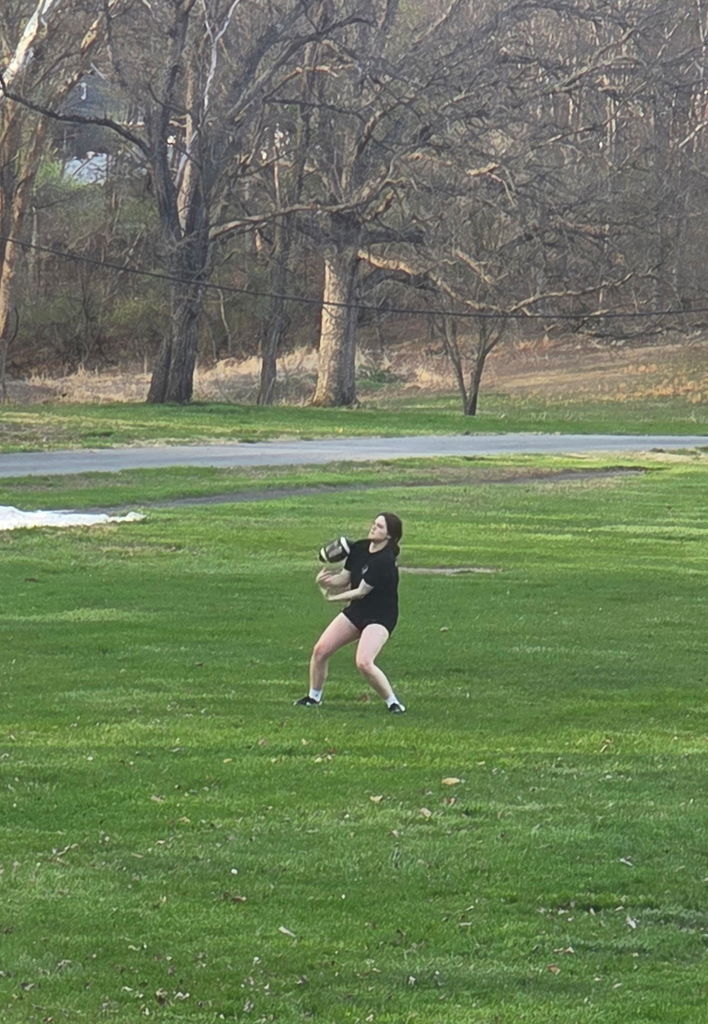 A female student wearing matching black shorts and top gets ready to catch a football.