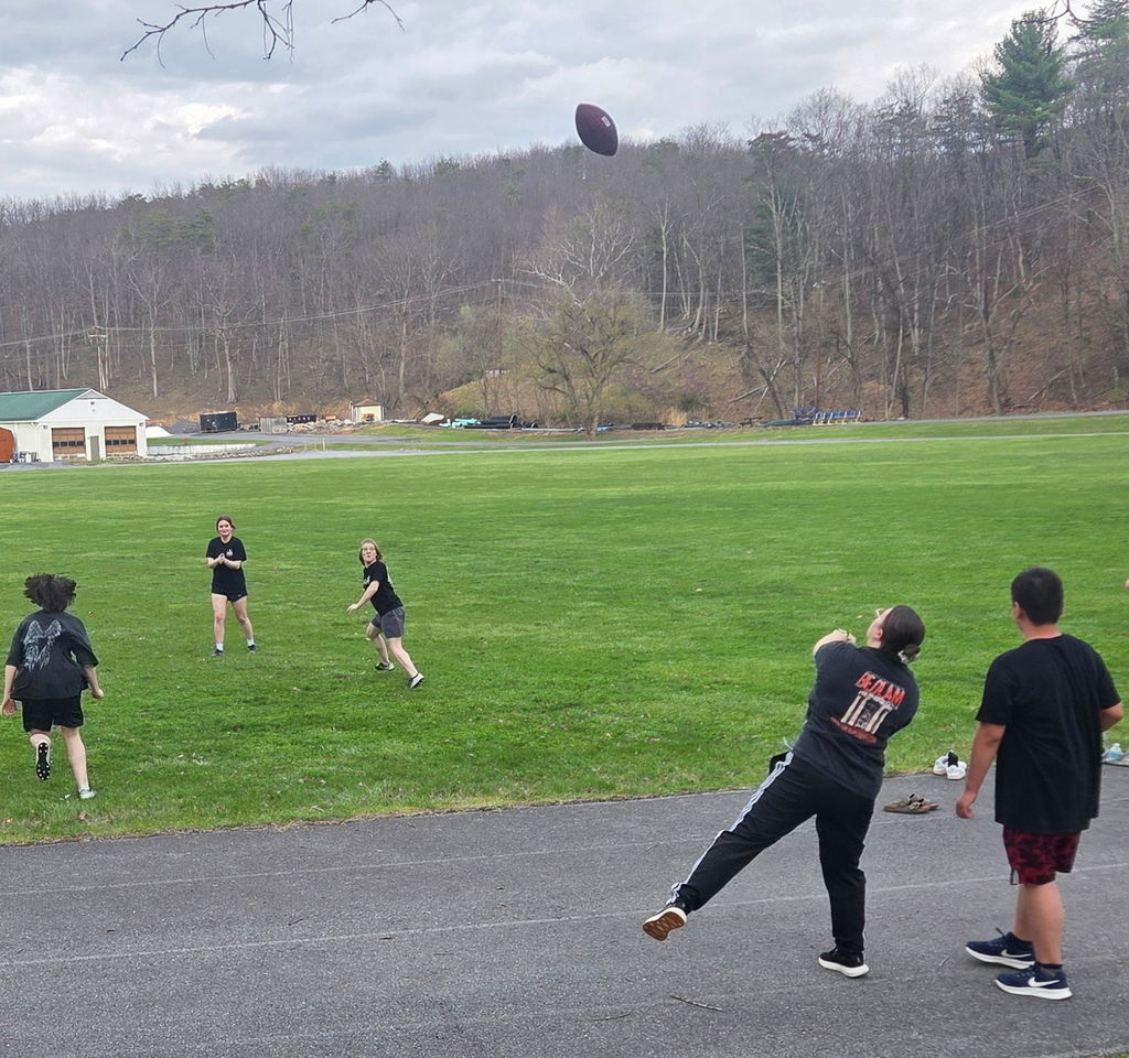 A female coach throws a football while a group of female students run to receive the football.
