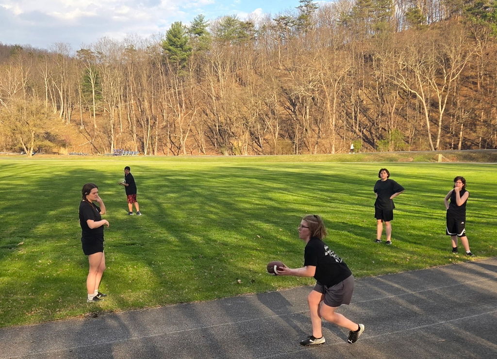 A group of female students wearing matching black tops and shorts stand in a group passing around a football.