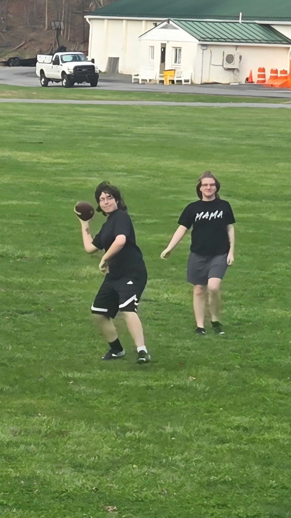 Two female students wearing a black top and shorts stand side-by-side. The female on the left gets ready to throw a football.