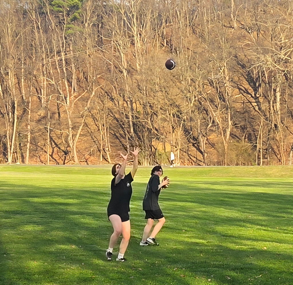 Two female students wearing matching black outfits rush to catch a football.