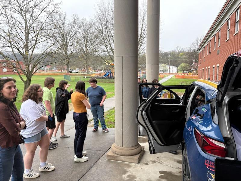 Students gathered around a blue-colored vehicle as they observe the vehicle and its features.