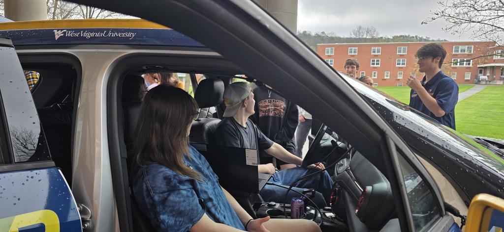 Two students are seated in the drivers and passenger seats of the ECOCar.