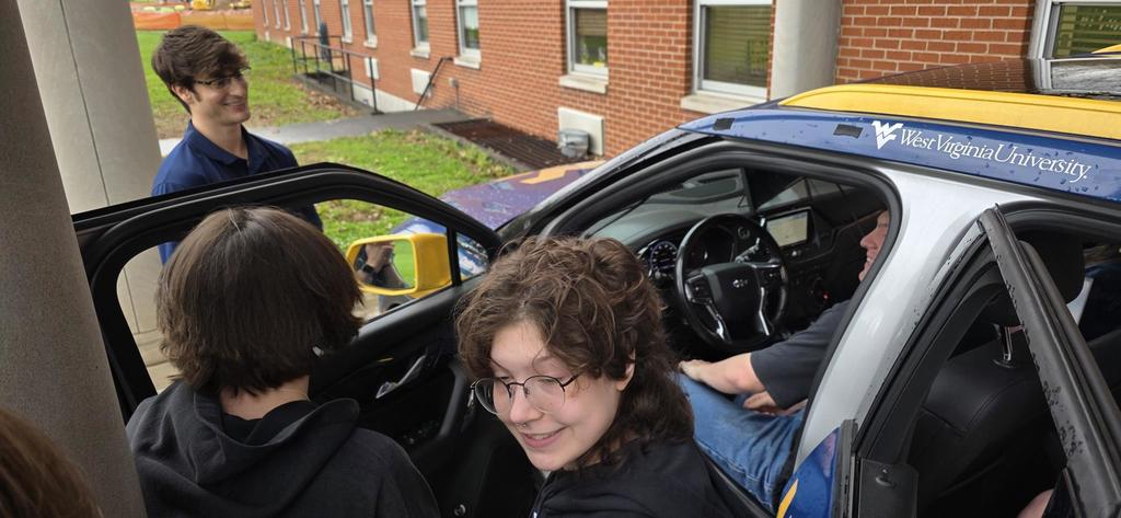 Students look inside of the ECOCar while a male student is in the driver's seat of the vehicle.
