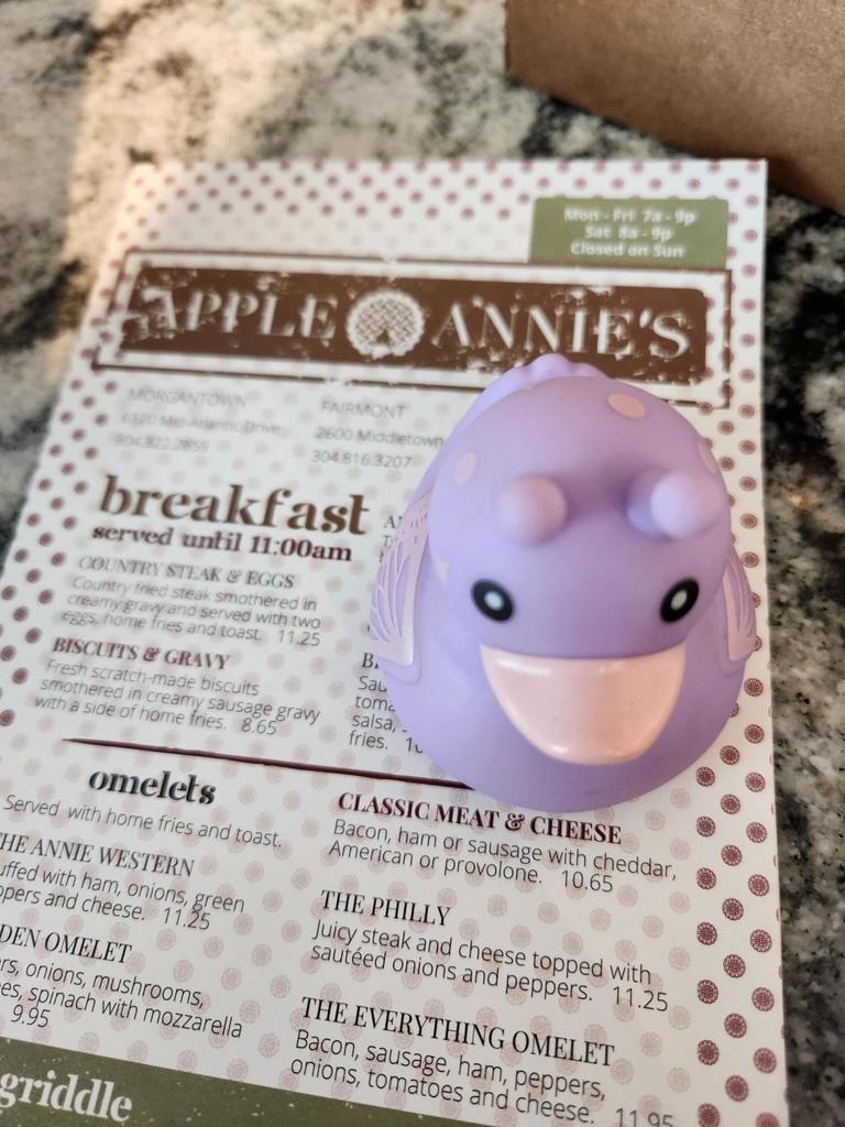 A purple rubber duck sits on top of a restaurant menu. Menu items are in black font.