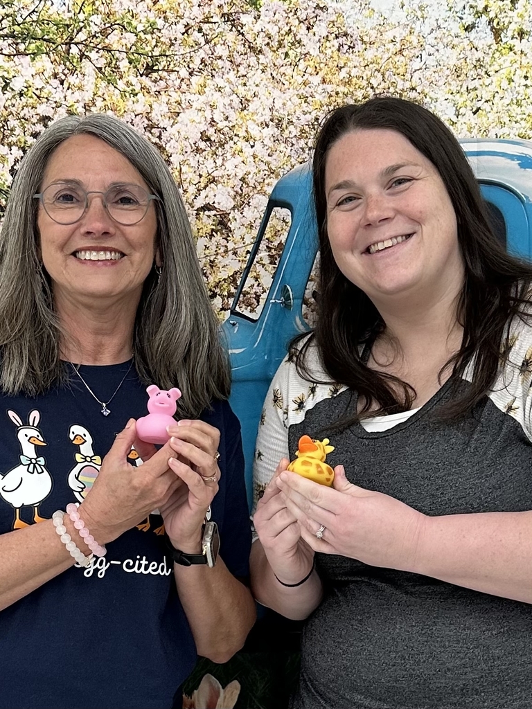 Two females stand side-by-side smiling at the camera while both are holding up rubber ducks.