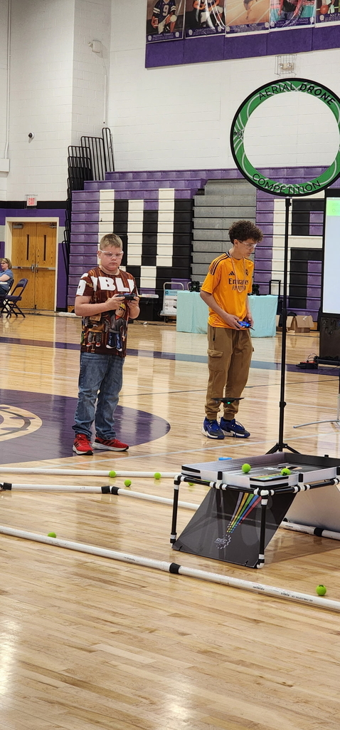 Two male drone competitors stand alongside one another, both holding controllers as they compete against one another.