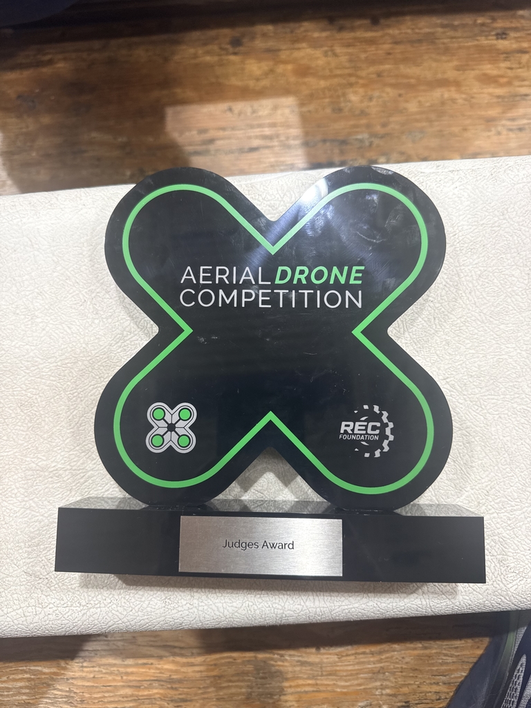 A green and black trophy in the shape of an "X" with the text "Aerial Drone Competition." and "Judges Award" at the bottom engraved in silver.