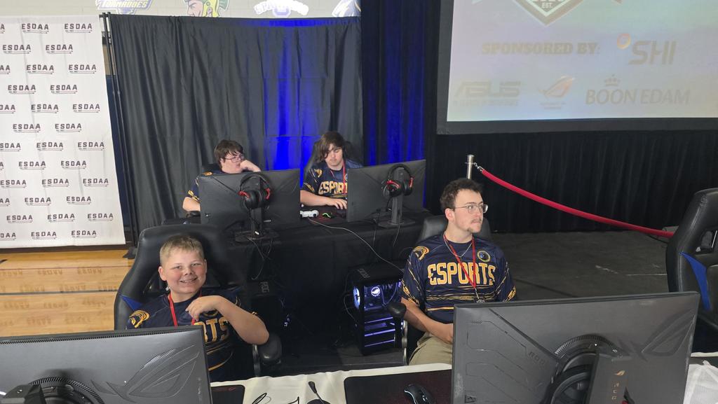 Four male Esports athletes wearing matching jerseys sit at their gaming stations.