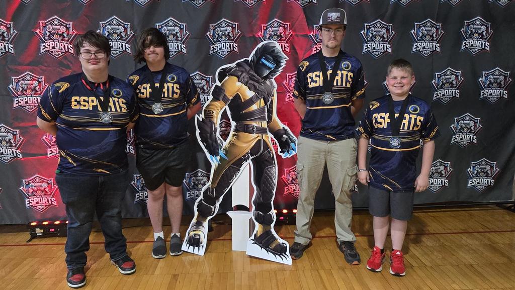 Four male team members dressed in matching jerseys pose with a cardboard cutout of a video game character.