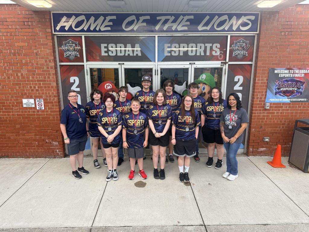 Group photo of the WVSDB Esports team dressed in matching blue and yellow jerseys. Coach Ganoe and Carr are on each side of the group.