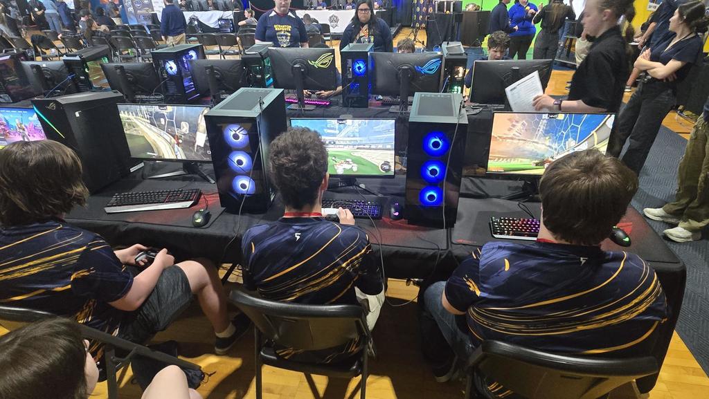 Three male Esports players wearing matching jerseys sit side-by-side as they compete in the tournament.