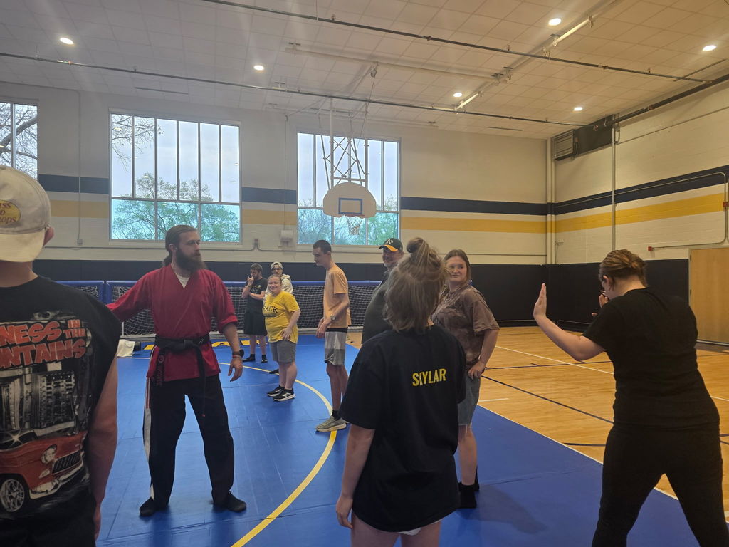 Students and Martial Arts instructors on a blue mat practice techniques they have been taught.
