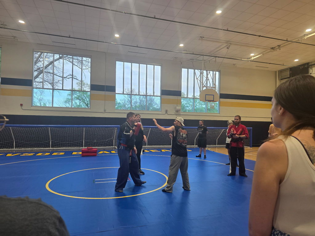 Martial Arts instructors standing on a blue mat with students as they teach them self-defense techniques.