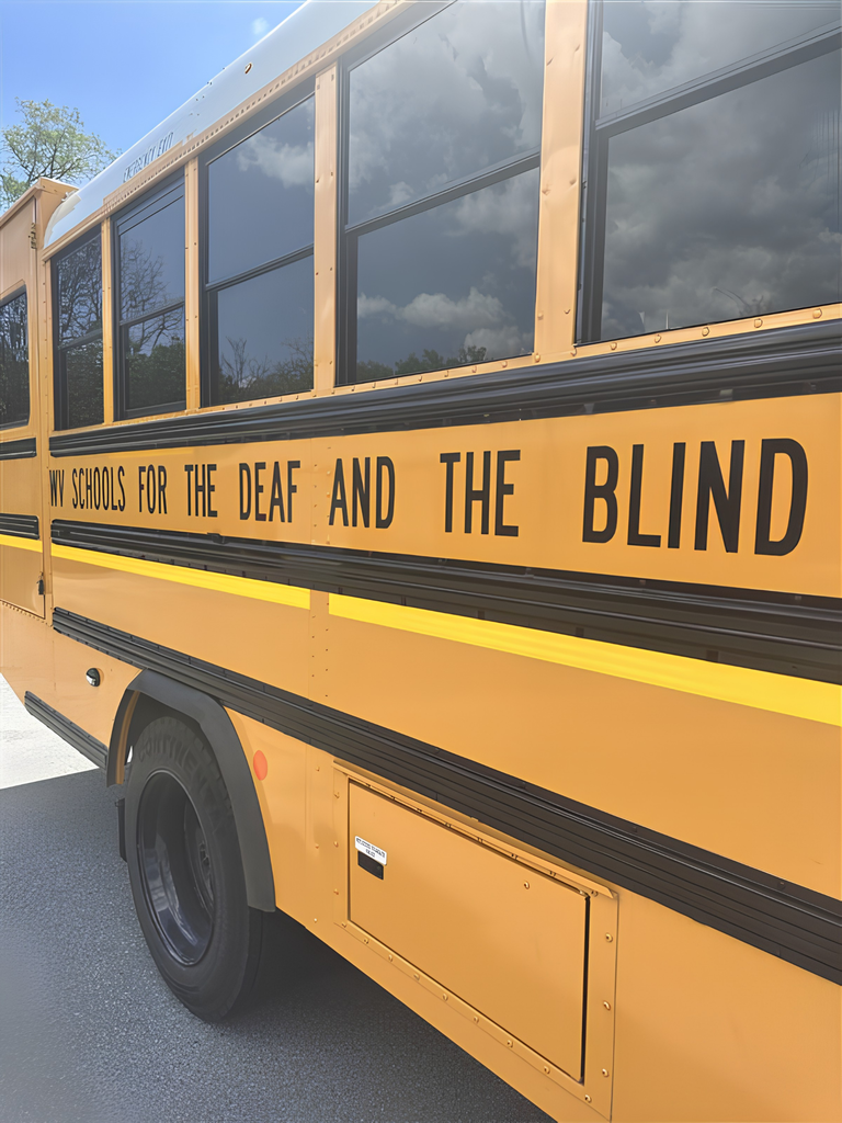 The back end of a yellow school bus with "West Virginia Schools for the Deaf and the Blind" in bold, black font.