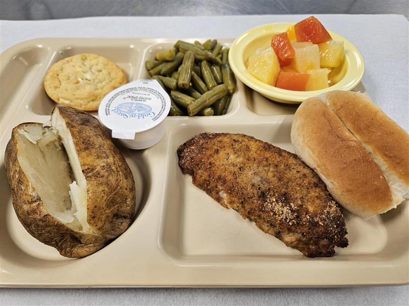 Student lunch tray consisting of chicken, fruit, green beans, a baked potato, and a cookie.