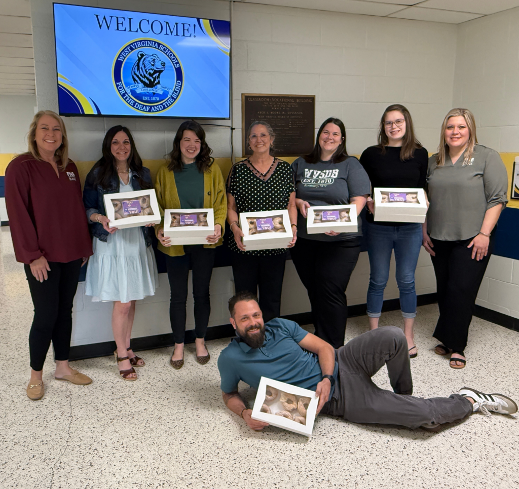 A group of WVSDB staff stand side-by-side FNB Bank Employees. WVSDB staff members are holding boxes of donuts.