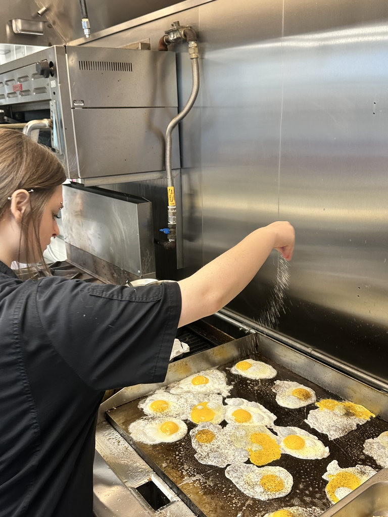 A female culinary student, Bray, sprinkles salt onto eggs cooking on a stovetop.