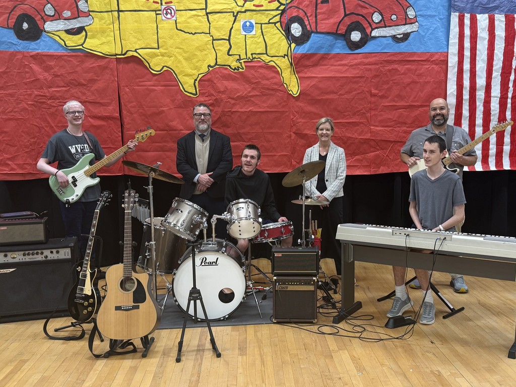 Superintendent Michele Blatt and Associate Superintendent Jeff Kelly stand among WVSDB Rock Band members and Mr. Haza on stage in an auditorium.