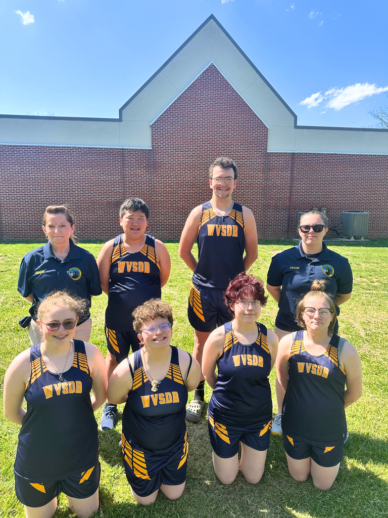 The Co-Ed WVSDB Track team posing in two rows- a front row and a back row. They are wearing matching blue and yellow uniforms. Coach See and Coach Mongold are on either side of the athletes.