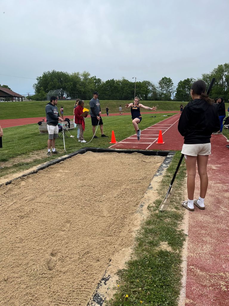 A female athlete, Skylar runs and is getting ready to do the long jump and land in a sand pit.