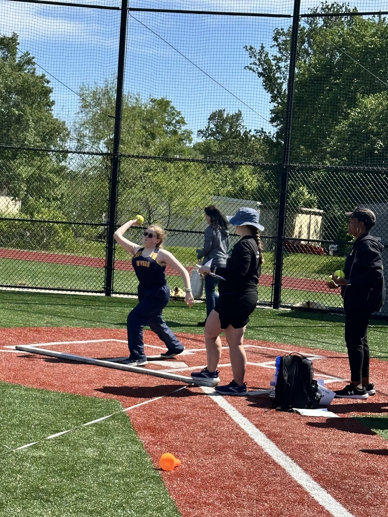 A female athlete, Brooklyn, gets ready to throw a neon yellow softball during a field event.