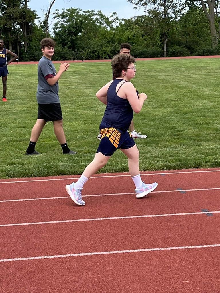 A female athlete, Willow, dressed in a blue and yellow uniform runs as individuals in the background cheer for her.