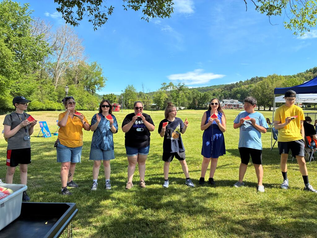 A group of participants stand in a line, side-by-side while posing with a piece of watermelon.
