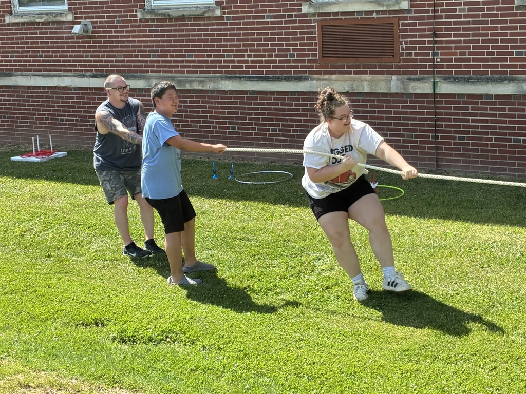 Three individuals are pulling on a rope during an outdoor game.