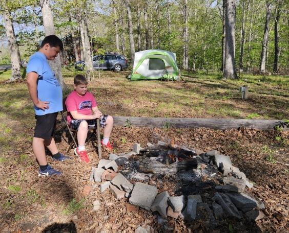 Tristian and Aiden observe a campfire There is a green and white tent in the background.