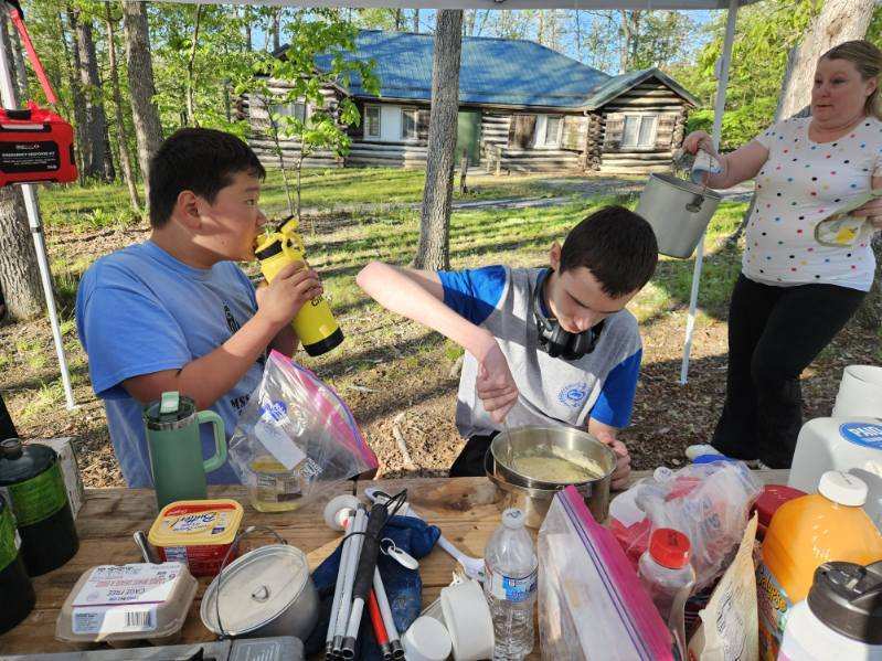 Wyatt stirs together pancake batter in a silver bowl. Alongside Wyatt are Tristian and their Troop Leader.
