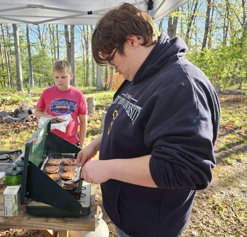 Carson looks down at a grill while he cooks sausages.