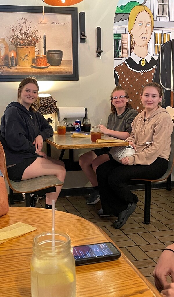 Bray, Madison, and Skylar are seated at a booth inside of a restaurant.