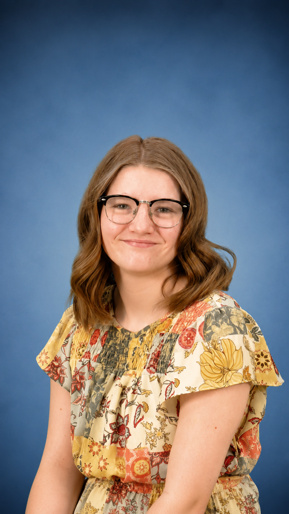 Skylar Lanham. Skylar smiles at the camera. She is wearing a floral top with multiple colors. She is seated in front of a navy-colored backdrop.