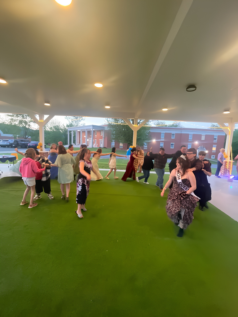 WVSDB students dressed in formal attire in a line, dancing under the outdoor pavilion. Keller Hall is in the background.