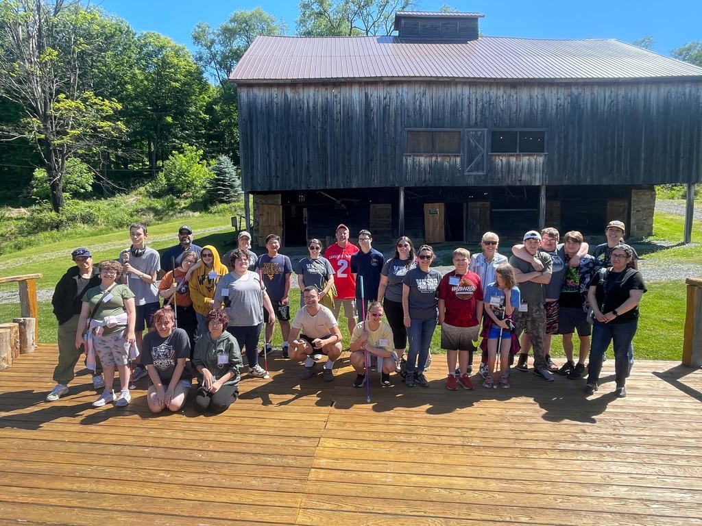 Group photo of students and chaperones stand on a wooden structure with an old, wooden barn in the background.