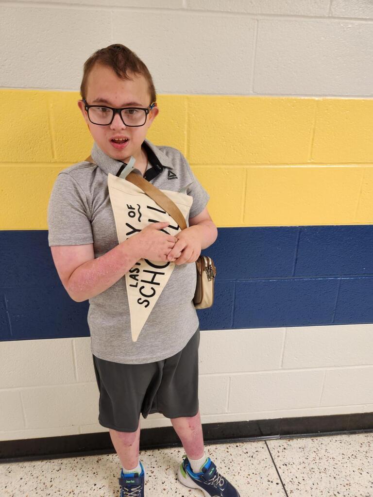 Jayden, a male student, holds up a beige-colored pennant flag with black text "Last Day of School."