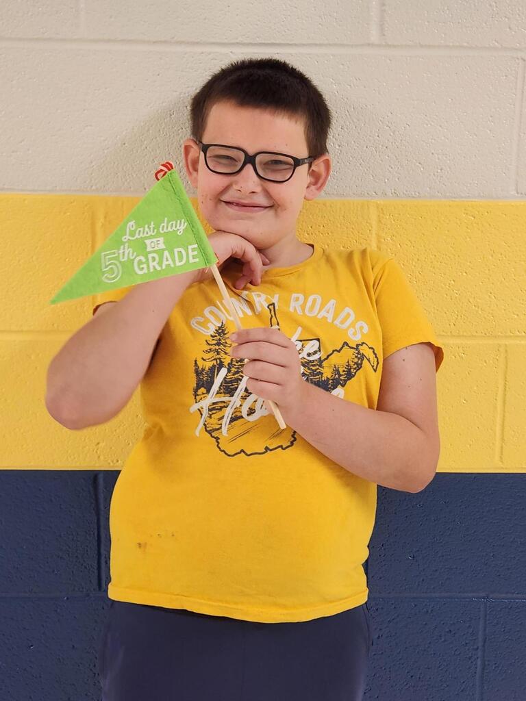 Landon, a male student holds up a green colored flag with white text "Last Day of 5th Grade."