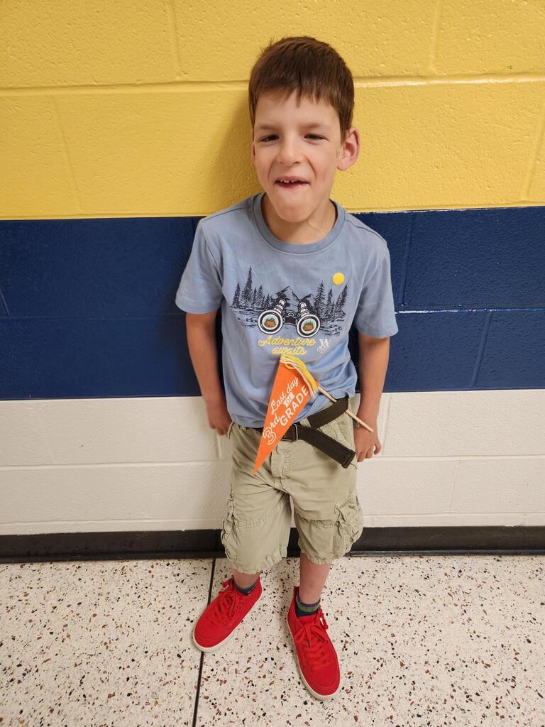 Dexter, a male student holds an orange flag with text "Last Day of 3rd Grade."